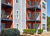 Thumbnail 2 of 25 - A modern two-story apartment building with red accents on the balconies and doors at Infinity on the Landing Apartments, Texas