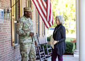 Thumbnail 5 of 74 - A man in military uniform stands outside a building talking to a woman.