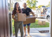 Thumbnail 7 of 37 - A man and a woman are carrying a box out of a house.