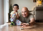 Thumbnail 12 of 37 - A man and a child are sitting on the floor playing with a toy.
