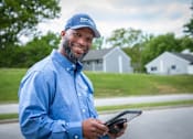Thumbnail 17 of 37 - A man in a blue shirt and cap is holding a tablet.