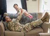 Thumbnail 20 of 37 - A man in military uniform is lying on a couch with a baby on his feet.