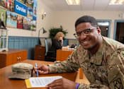 Thumbnail 23 of 37 - A soldier in uniform is signing a document at a desk.