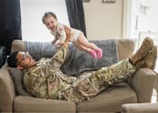 Thumbnail 10 of 74 - A man in military uniform lying on couch lifting child up.