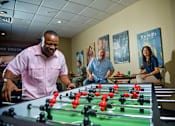 Thumbnail 28 of 74 - A man in a pink shirt is playing foosball with two other people.