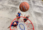 Thumbnail 3 of 21 - A basketball player in a blue jersey is attempting to block a shot by a player in a black jersey.