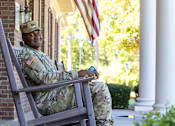 Thumbnail 10 of 21 - A soldier in uniform sits on a porch swing.