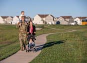 Thumbnail 19 of 21 - A man in military uniform pushes a stroller with a child in it while a woman walks beside them.