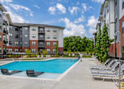 Thumbnail 3 of 69 - A swimming pool surrounded by lounge chairs in front of a multi-story apartment building.