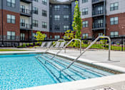 Thumbnail 2 of 69 - A swimming pool in front of a multi-story apartment building.