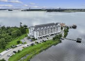 Thumbnail 5 of 25 - A large white building with a grey roof is surrounded by water and greenery.