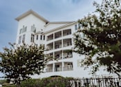 Thumbnail 4 of 25 - A white building with balconies and windows is surrounded by trees.