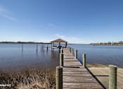 Thumbnail 12 of 25 - A wooden pier extends into a calm body of water under a clear blue sky.