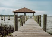 Thumbnail 11 of 25 - A wooden pier leads to a gazebo in the middle of a body of water.