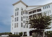 Thumbnail 2 of 25 - A white building with a balcony on the second floor.