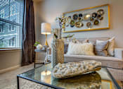 Thumbnail 9 of 36 - A living room with a grey couch, a glass table, and a large picture frame on the wall.