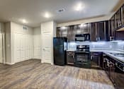 Thumbnail 16 of 36 - A kitchen with wooden floors and black appliances.
