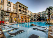 Thumbnail 33 of 36 - A large swimming pool surrounded by lounge chairs in front of apartment buildings.