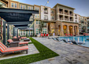 Thumbnail 30 of 36 - A pool area with lounge chairs and a building in the background.