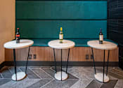 Thumbnail 11 of 30 - Three small tables with wine bottles on them.