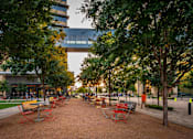 Thumbnail 21 of 30 - A park with benches and trees in front of a building.