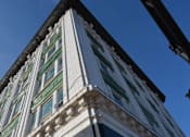 Thumbnail 10 of 14 - A tall building with a green awning is seen from below.