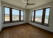 Thumbnail 3 of 14 - A room with wooden floors and two windows overlooking a parking lot.
