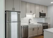 Thumbnail 21 of 25 - A modern kitchen with a stainless steel refrigerator and white countertops.