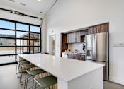 Thumbnail 28 of 36 - A modern kitchen with a long white counter and a refrigerator.