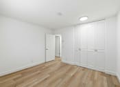 Thumbnail 82 of 133 - A room with white walls and wooden flooring with a door on the left and a set of white cupboards on the right.
