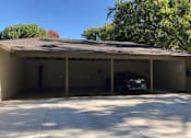 Thumbnail 23 of 47 - A black car is parked in a garage with a tree in the background.