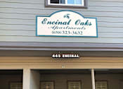 Thumbnail 12 of 22 - A silver car is parked in front of a building with a sign that says Encinal Oaks Apartments.