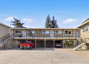 Thumbnail 3 of 17 - A red car is parked in the garage of a two-story apartment building.