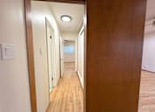 Thumbnail 7 of 33 - A long hallway with wooden floors and white walls.