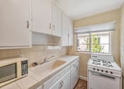 Thumbnail 16 of 21 - A kitchen with a white stove, sink, and microwave.