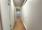 Thumbnail 18 of 33 - A long hallway with wood floors and white walls.