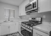 Thumbnail 15 of 31 - A black and white photo of a kitchen with a stove, microwave, and cabinets.