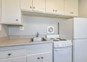 Thumbnail 33 of 42 - A white kitchen with a stove, sink, and cabinets.