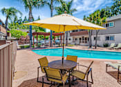 Thumbnail 2 of 25 - A yellow umbrella shades a table with chairs around a pool.