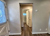 Thumbnail 25 of 50 - A hallway with a white door and a window with blinds on the left.