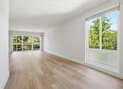 Thumbnail 77 of 92 - A room with wooden flooring and a large window overlooking a green outdoor area.