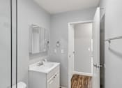Thumbnail 39 of 40 - A white bathroom with a sink, mirror, toilet, and a door.