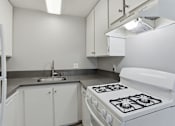 Thumbnail 44 of 55 - A white kitchen with a stove, sink, and cabinets.