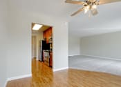 Thumbnail 23 of 37 - A room with a ceiling fan and a kitchen area in the background.
