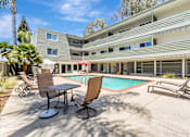 Thumbnail 17 of 43 - A pool area with chairs and a table in front of a building.