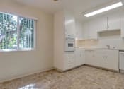 Thumbnail 17 of 34 - A kitchen with white cabinets and a window with trees outside.