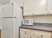 Thumbnail 40 of 43 - A white refrigerator stands next to a counter with a microwave on it.