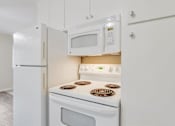 Thumbnail 29 of 37 - A white kitchen with a stove, microwave, and refrigerator.
