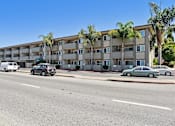 Thumbnail 2 of 27 - A street view of a residential building with cars parked in front.