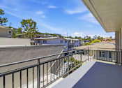 Thumbnail 47 of 92 - A balcony with a metal railing overlooks a parking lot and buildings.